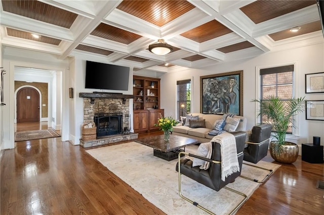 living room featuring arched walkways, a stone fireplace, wood finished floors, and beam ceiling