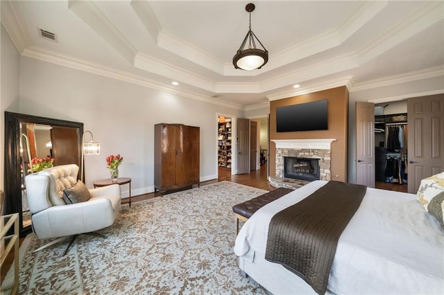 bedroom featuring visible vents, a raised ceiling, wood finished floors, and a stone fireplace