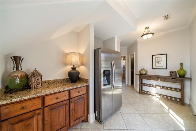 kitchen featuring visible vents, ornamental molding, light stone countertops, brown cabinetry, and stainless steel fridge