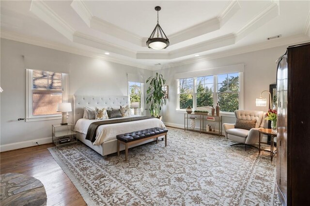 bedroom with wood finished floors, multiple windows, a raised ceiling, and crown molding