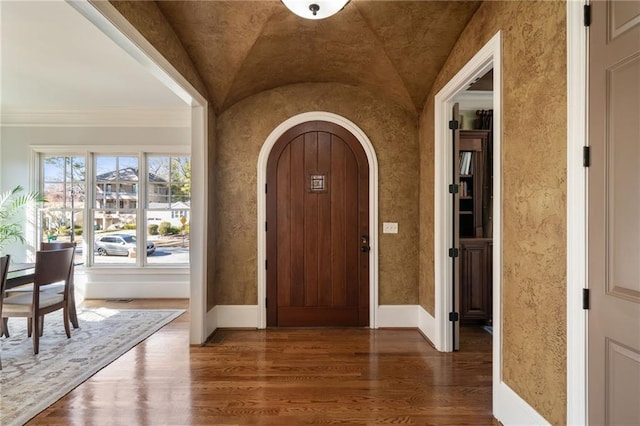 foyer featuring baseboards, arched walkways, vaulted ceiling, and wood finished floors