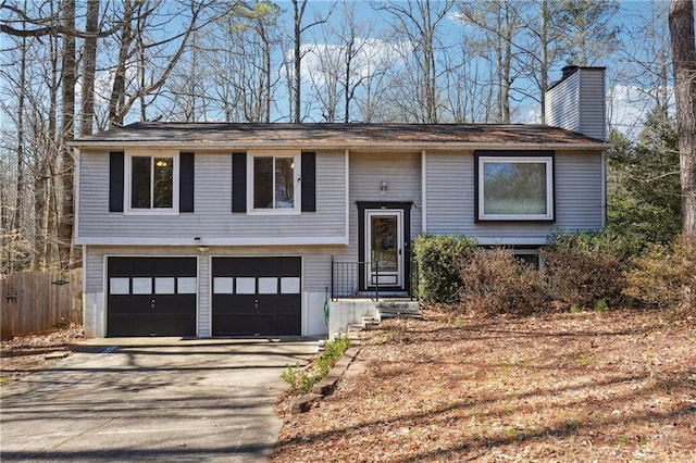 split foyer home with fence, a chimney, driveway, and an attached garage