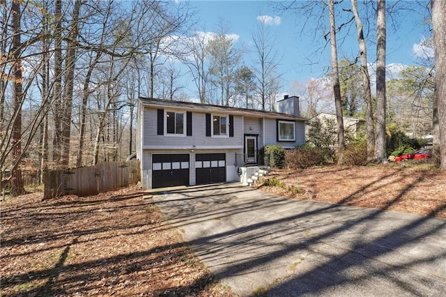 raised ranch featuring fence, a chimney, aphalt driveway, and a garage