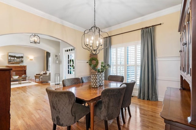 dining space with an inviting chandelier, crown molding, light wood-style flooring, and arched walkways