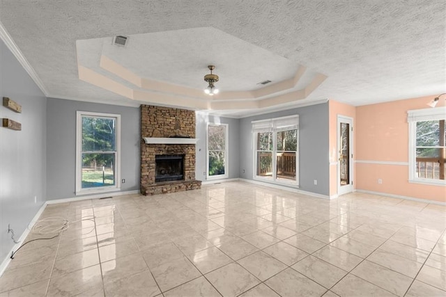 unfurnished living room featuring a textured ceiling, a stone fireplace, crown molding, and a tray ceiling