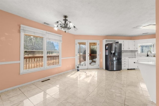 kitchen with dishwasher, white cabinetry, sink, stainless steel fridge, and a notable chandelier