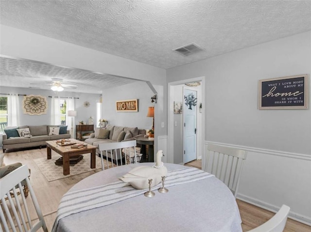 dining space with light wood-style floors, ceiling fan, and a textured ceiling