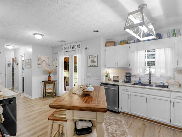 kitchen with stainless steel dishwasher, a sink, light wood-style floors, a wainscoted wall, and white cabinets