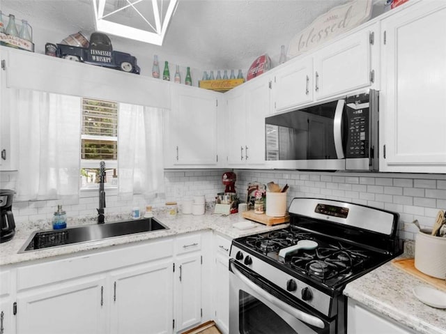 kitchen featuring appliances with stainless steel finishes, a sink, white cabinets, decorative backsplash, and a textured ceiling