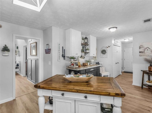 kitchen with open shelves, white cabinets, light wood-style floors, butcher block counters, and a textured ceiling