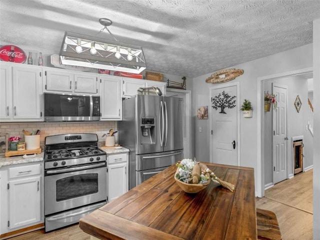kitchen with appliances with stainless steel finishes, tasteful backsplash, light wood finished floors, a textured ceiling, and white cabinetry