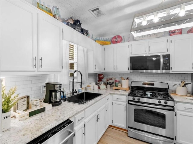kitchen featuring appliances with stainless steel finishes, a sink, white cabinets, and tasteful backsplash
