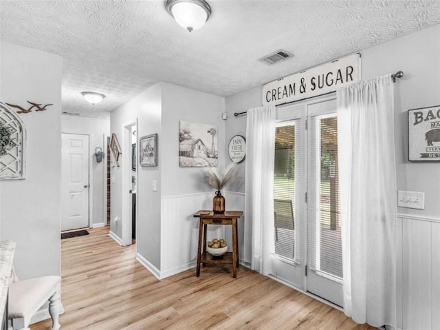 entrance foyer with wood finished floors, a textured ceiling, and wainscoting