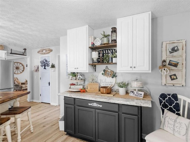 kitchen with a textured ceiling, light wood-style flooring, freestanding refrigerator, open shelves, and white cabinets