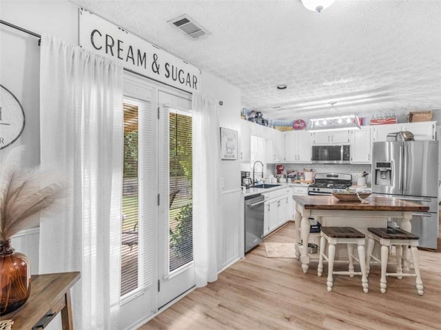 kitchen featuring appliances with stainless steel finishes, a sink, a textured ceiling, a kitchen island, and light wood-style floors