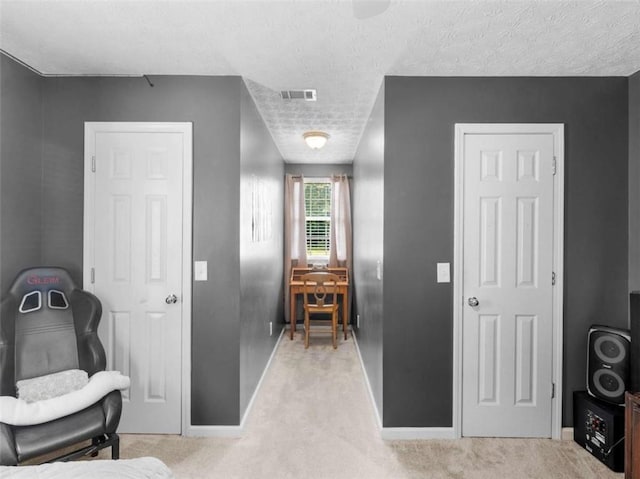 hallway featuring baseboards, light colored carpet, and a textured ceiling
