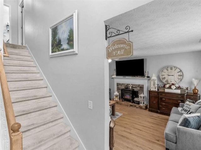living area featuring stairs, a textured ceiling, wood finished floors, and a fireplace