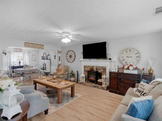 living room featuring ceiling fan, wood finished floors, a wood stove, and a textured ceiling