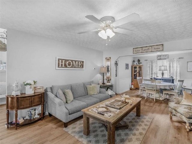 living area featuring light wood-type flooring, a textured ceiling, and ceiling fan
