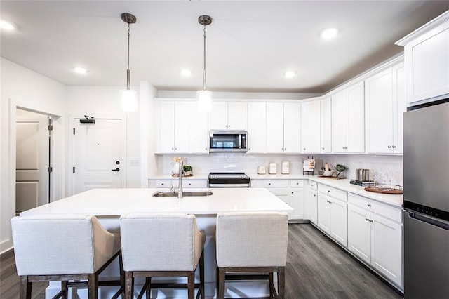 kitchen with tasteful backsplash, dark wood-type flooring, appliances with stainless steel finishes, sink, and a center island with sink