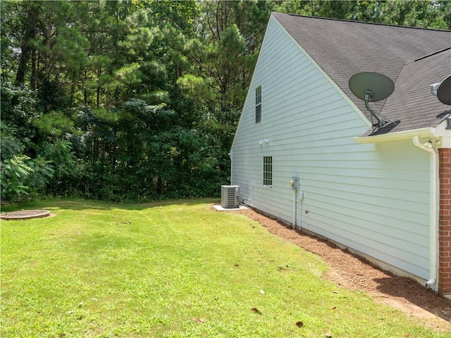 view of side of property featuring central air condition unit, roof with shingles, and a yard