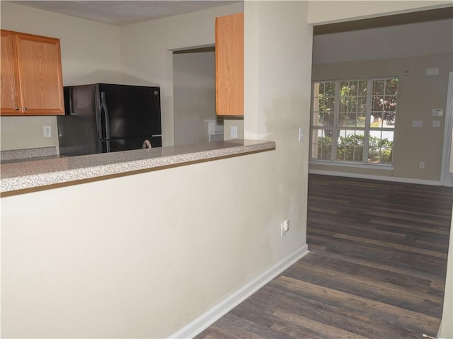 kitchen with dark wood-style flooring, brown cabinets, light countertops, freestanding refrigerator, and baseboards