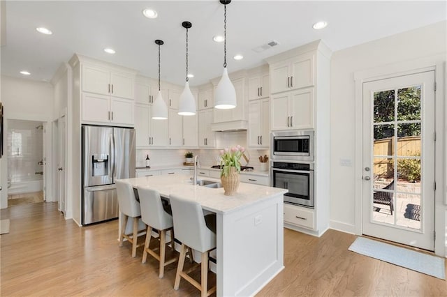 kitchen featuring hanging light fixtures, white cabinetry, appliances with stainless steel finishes, and a kitchen island with sink