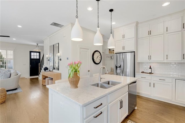 kitchen with appliances with stainless steel finishes, decorative light fixtures, white cabinetry, an island with sink, and sink