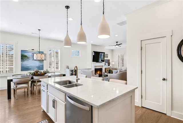 kitchen with sink, a kitchen island with sink, hanging light fixtures, white cabinets, and stainless steel dishwasher