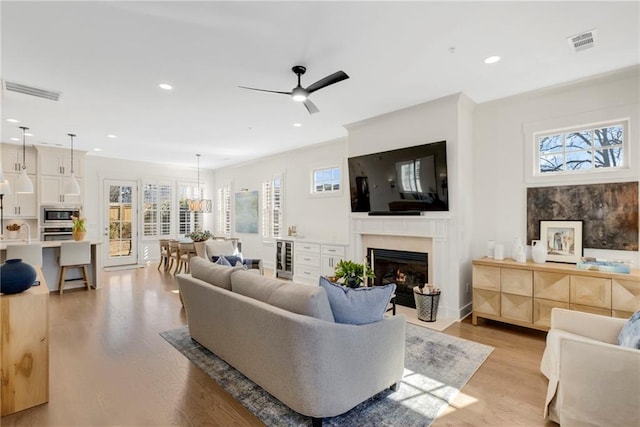 living room featuring wine cooler, sink, ceiling fan, a high end fireplace, and light hardwood / wood-style floors