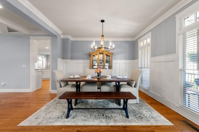 dining room with a wainscoted wall, visible vents, ornamental molding, a chandelier, and light wood-style flooring