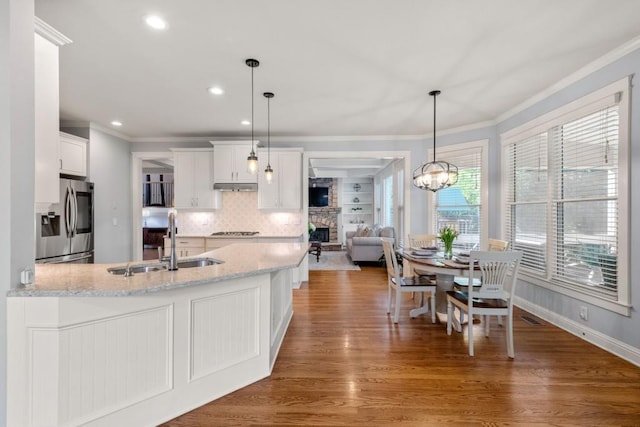 kitchen with stainless steel fridge with ice dispenser, ornamental molding, a sink, a peninsula, and a fireplace