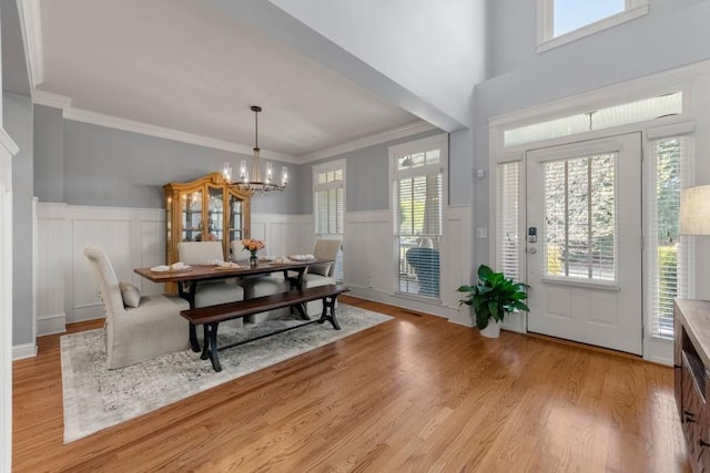 entryway with wainscoting, an inviting chandelier, light wood-type flooring, and crown molding