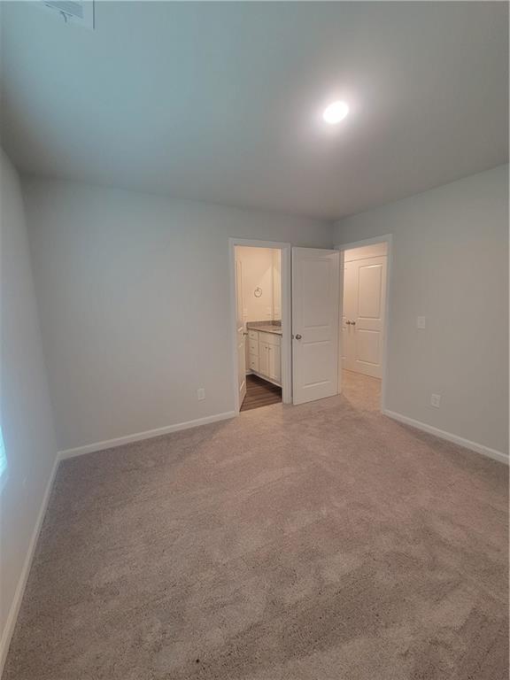 unfurnished bedroom featuring carpet floors, baseboards, and ensuite bathroom