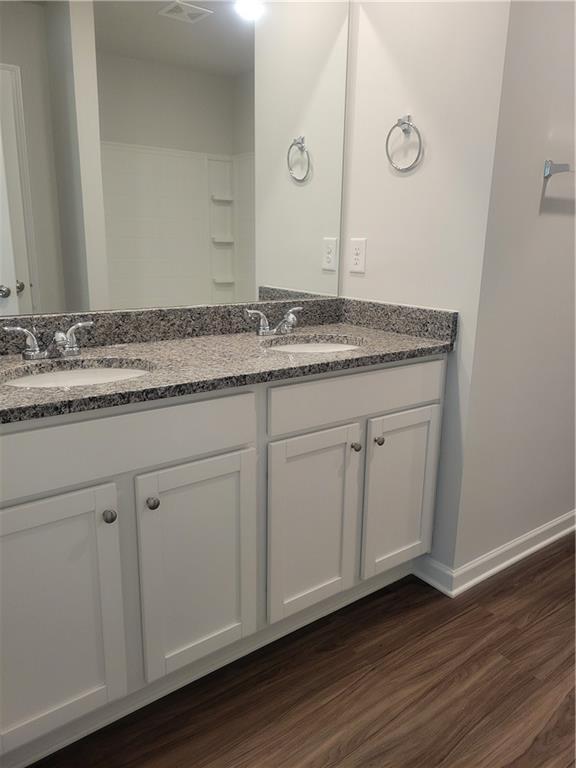 full bathroom featuring double vanity, a sink, baseboards, and wood finished floors