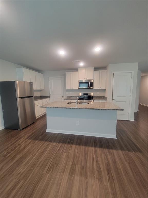 kitchen featuring white cabinets, light stone countertops, appliances with stainless steel finishes, and dark wood-type flooring