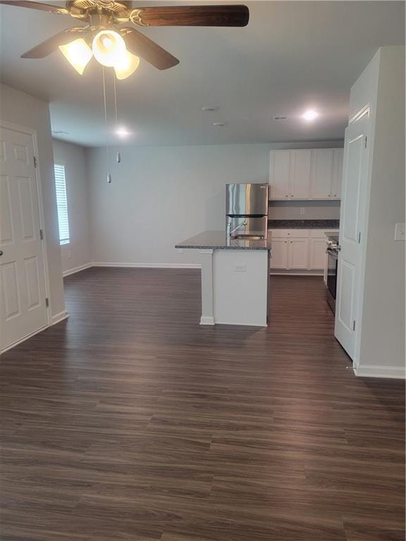 kitchen featuring white cabinets, dark countertops, freestanding refrigerator, a ceiling fan, and baseboards
