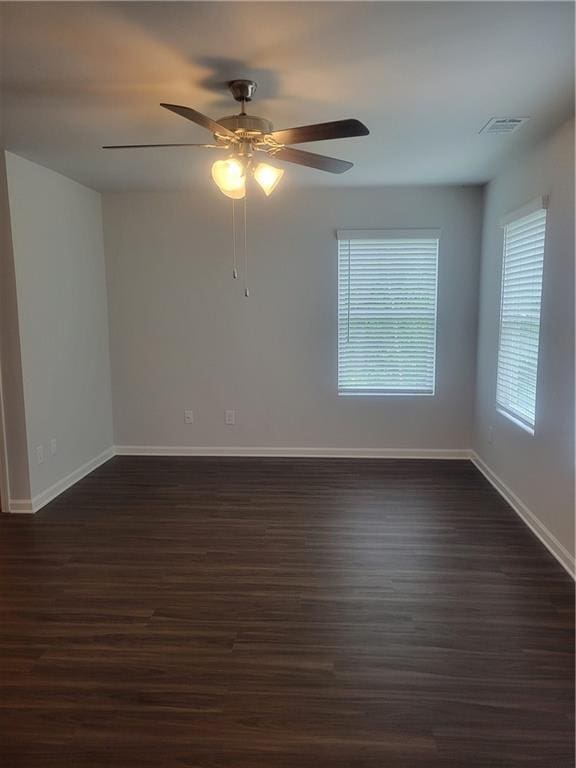 spare room with baseboards, visible vents, a ceiling fan, and dark wood-type flooring