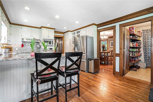 3392 Inns Brook Way, Snellville, GA 30039 - kitchen with appliances with stainless steel finishes, a peninsula, ornamental molding, tasteful backsplash, and white cabinets