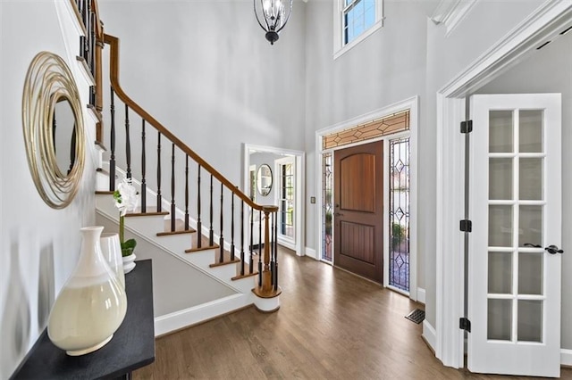 entrance foyer with wood finished floors, baseboards, an inviting chandelier, a high ceiling, and stairs