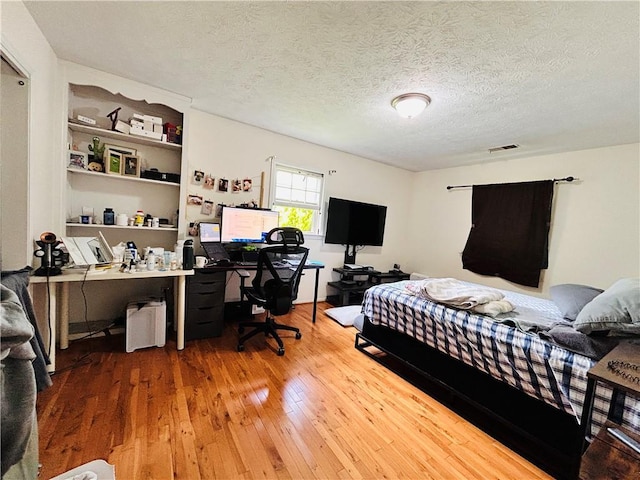 bedroom featuring an office area, hardwood / wood-style floors, and a textured ceiling