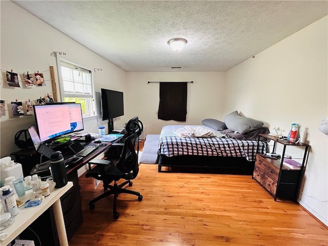 bedroom with light wood finished floors, an office area, and a textured ceiling