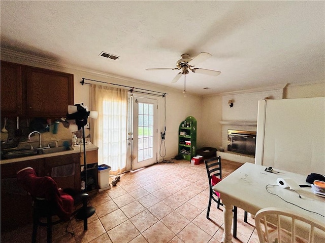 kitchen featuring a sink, a glass covered fireplace, ceiling fan, ornamental molding, and light tile patterned flooring