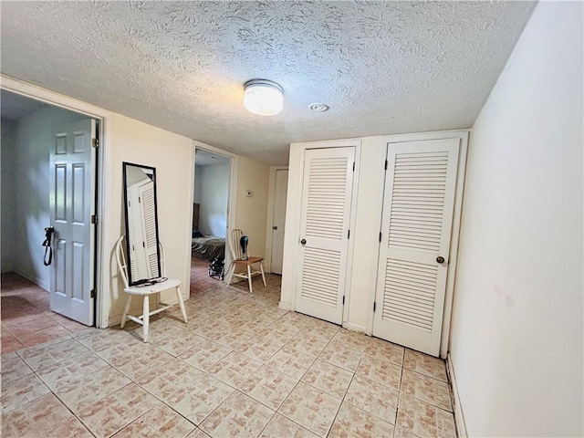 bedroom with multiple closets, light tile patterned floors, baseboards, and a textured ceiling