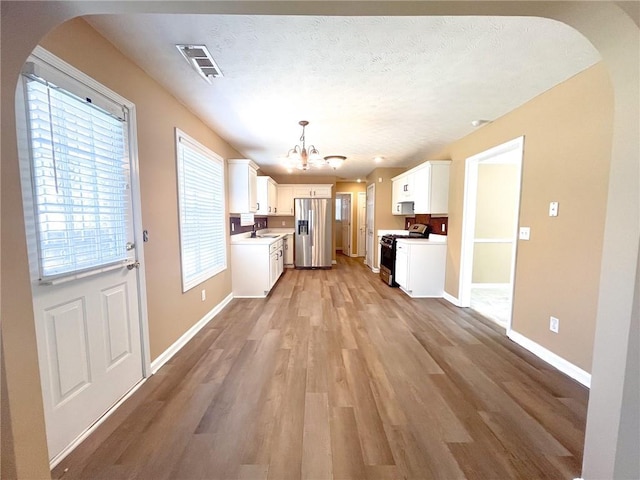 kitchen with an inviting chandelier, arched walkways, gas stove, a sink, and stainless steel fridge