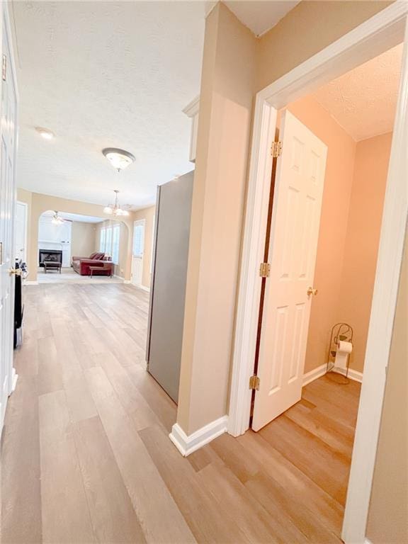 hallway with arched walkways, baseboards, and light wood-style floors