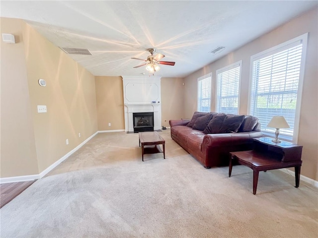 living area featuring light colored carpet, a ceiling fan, baseboards, a fireplace with flush hearth, and visible vents