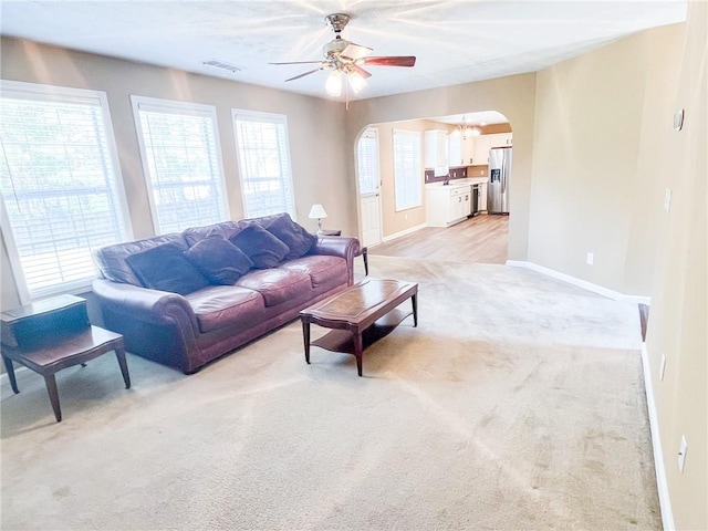 living room with visible vents, light carpet, baseboards, arched walkways, and ceiling fan with notable chandelier
