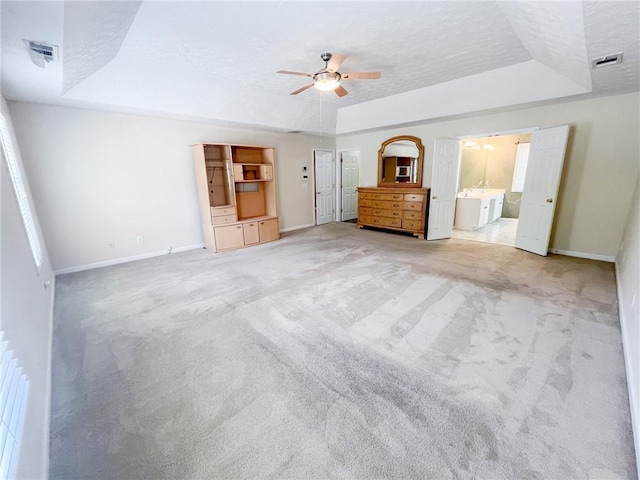 unfurnished bedroom with ceiling fan, light colored carpet, a textured ceiling, baseboards, and a tray ceiling