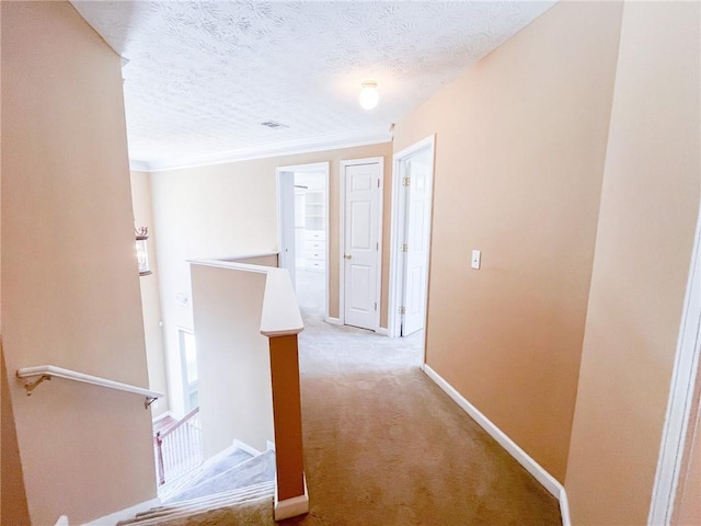 corridor featuring ornamental molding, light carpet, baseboards, a textured ceiling, and an upstairs landing